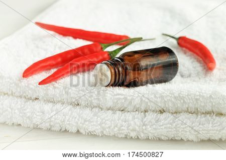 Red pepper tincture in dropper bottle on white towel, little bright pods. Hair care natural remedy.