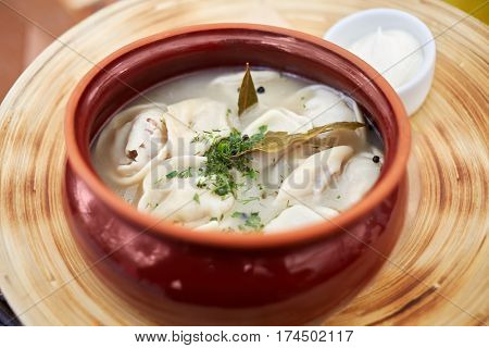 Ceramic pot with boiled pelmeni and bowl with sauce.
