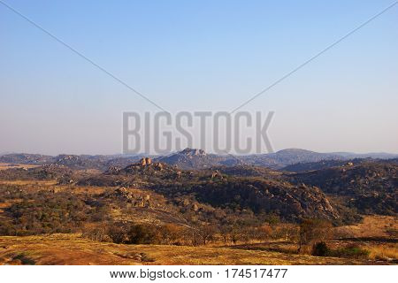a wide panorama of the national park Matopos-Rhodes in Zimbabwe with the typical rock structures of naked big stones and some hills like also orange-red bushes