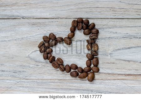 Roasted coffee beans in a shape of a heart on wooden background