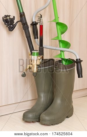 Fishing concept: fishing rods and hand ice drill in rubber boots
