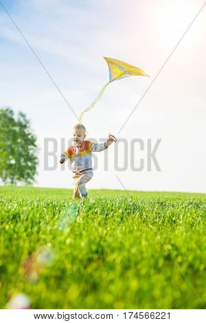 Young boy flies his kite in an open field. Little kid playing with kite on green meadow. Childhood concept.