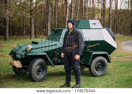 Pribor, Belarus - April 23, 2016: Re-enactor Dressed As Russian Soviet Crew Member Soldier Of World War II Standing At Armoured Soviet Scout Car BA-64 In Forest.