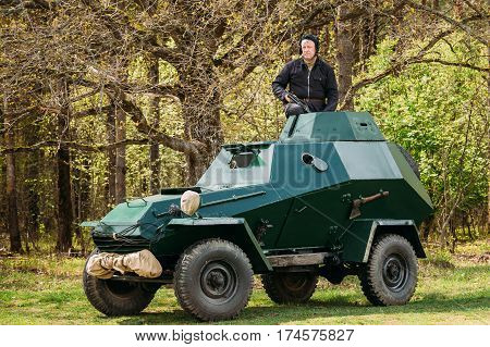 Pribor, Belarus - April 23, 2016: Re-enactor Dressed As Russian Soviet Crew Member Soldier Of World War II Sitting In Armoured Soviet Scout Car BA-64 In Forest.