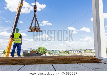 Crane hook with straps is raising palette on the unfinished hall.