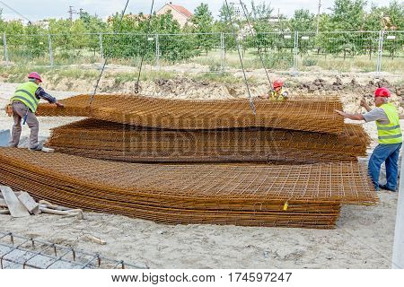Zrenjanin Vojvodina Serbia - June 29 2015: Team of riggers assist mobile crane to unload reinforcing mesh on pile. Workers are helping in manage the cargo.