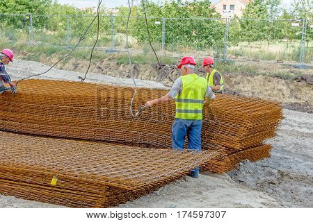 Zrenjanin Vojvodina Serbia - June 29 2015: Team of riggers assist mobile crane to unload reinforcing mesh on pile. Workers are helping in manage the cargo.