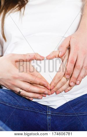 Pregnant Woman and Her Husband holding her hands in a heart shape on her baby bump. parents hands on her stomach Pregnant White T-shirt