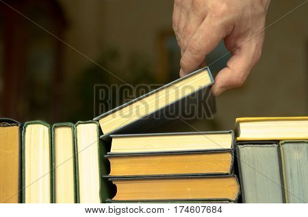 hand of man or woman takes a book on a shalf in the room or library