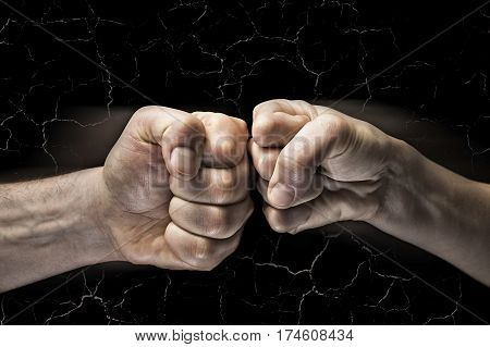 Image close up clash of two fists on black background with cracks. Concept of confrontation competition etc.