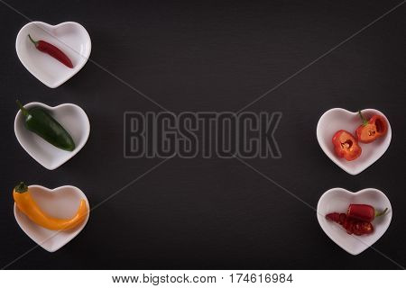 Different chili peppers on white plates, black stone background