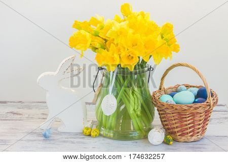 Easter eggs hunt - white rabbit, basket with painted blue eggs and daffodils bouquet