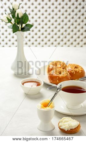 Delicious and healthy breakfast of boiled egg and brioche buns with black tea on a light background. Soft focus.