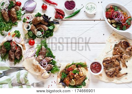 Tasty grilled meals frame on wood flat lay. Top view on assortment of hot bbq meat snacks, free space on white wooden table. Buffet, lunch, restaurant menu concept