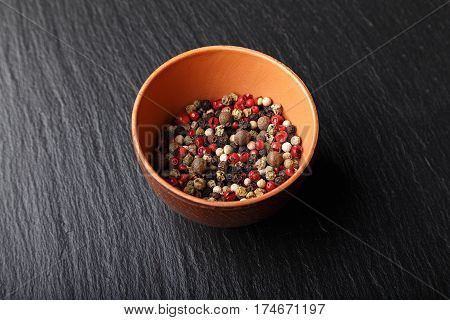 multicolored peppers peas in a clay cup on a slate boardHorizontal photo with free space area for text or design.