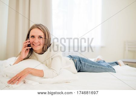 A woman lies forward on her bed making a call as she smiles