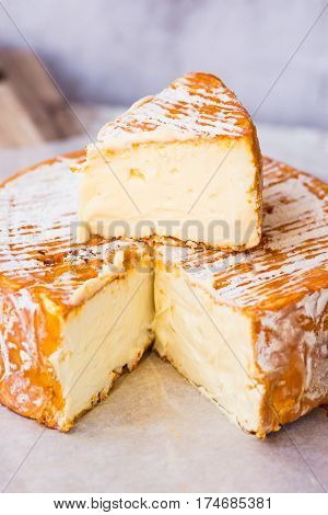 French German soft cheese with orange washed-rind on waxed paper on wood cutting board cut off slice close up rustic