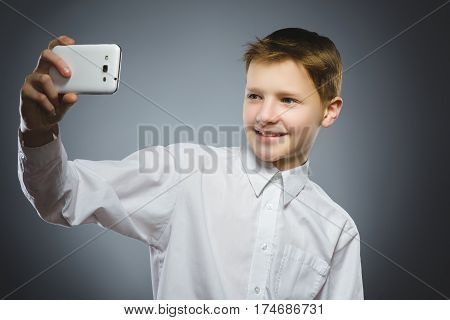 Closeup Portrait happy boy with mobile or cell phone making selfie on gray background