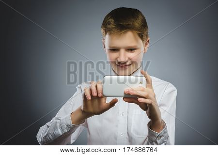 Closeup Portrait happy boy with mobile or cell phone making selfie on gray background