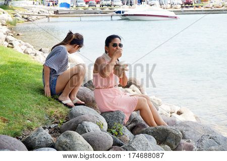 HARBOR SPRINGS, MICHIGAN / UNITED STATES - AUGUST 4, 2016: A woman eats Kilwin's chocolate ice cream, while sitting on a rock along the Harbor Springs waterfront, and enjoying the view of Little Traverse Bay.