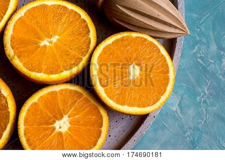 Ripe colorful oranges cut in half on stone platter with wood reamer by window top view close up natural light