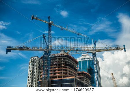 Cranes on modern skyscraper construction in city at sunny day with blue sky
