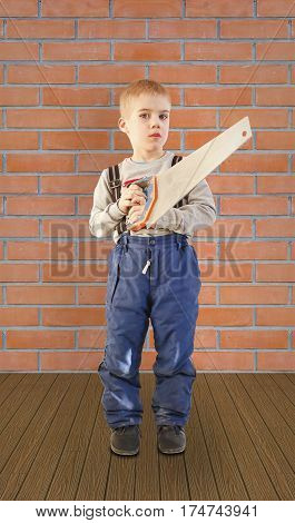 Boy child with the building tool. Is on the floor on brick wall background. The child worker the Builder. Saws with a saw. Holding the hand saw
