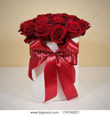 Rich gift bouquet of 21 red roses. Composition of flowers in a white hatbox. Tied with wide red ribbon and bow.