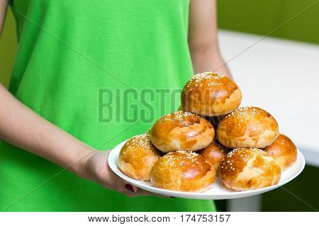 waitress in a green uniform holding a plate with fresh tasty buns with sesame in cafe