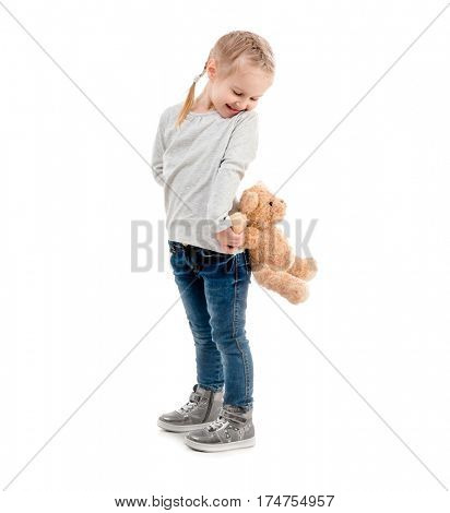 Small girl peaking on a teddy bear hidden behind her back, isolated on white background