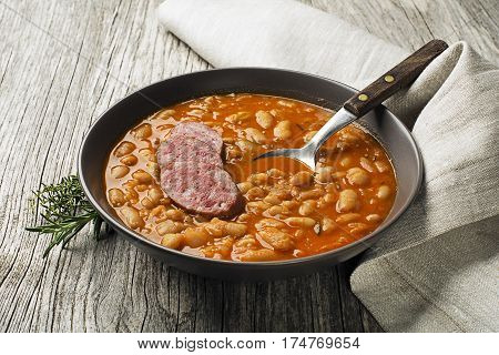 White bean stew with fresh spices and sausage on wooden table