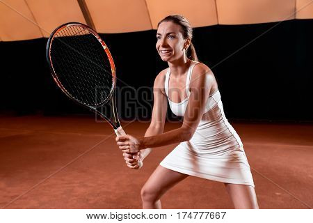 Sportswoman at the tennis court with racquet. Indoor tennis court