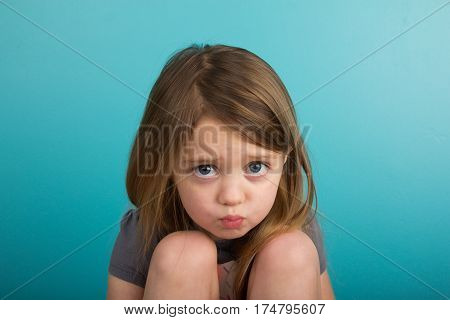 Little girl pouting against plain teal background