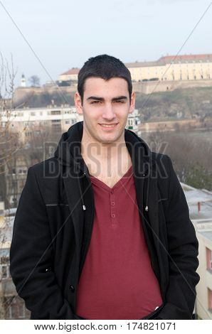 Photographing smiling Danila Mazić in a tight red shirt unbuttoned covered with a black coat and black pants a background Petrovaradin fortress and the Danube River, Novi Sad, Serbia