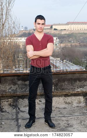 Photographing smiling Danila Mazić in a tight red shirt and black pants with arms folded in background Petrovaradin fortress and the Danube River, Novi Sad, Serbia