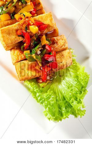 Tofu fritto conditi con verdure fritte. Guarnito con salsa e foglia di insalata fresca