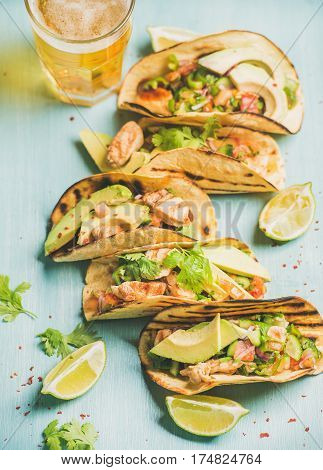 Healthy corn tortillas with grilled chicken, avocado, fresh salsa, limes and beer in glass over blue wooden background, selective focus. Gluten-free, allergy-friendly, weight loss, dieting concept