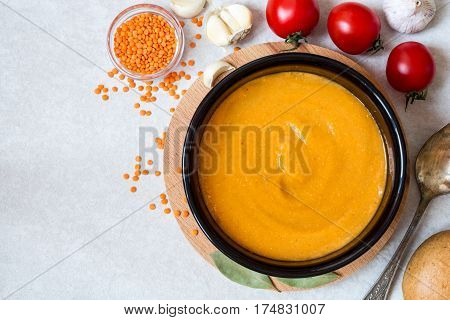 Red lentil cream soup in dark ceramic bowl on round cutting board. Grain lentils vegetables and bread. Vegetarian nutrition. Top view.