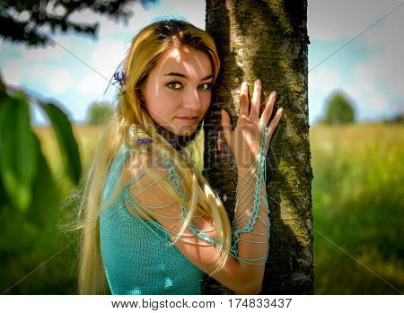 Young girl with long blond hair hugging tree trunk