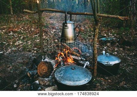 Old Retro Iron Camp Kettle And Pans Boils Water On A Fire In Forest. Bright Flame Fire Bonfire At Dusk Night.