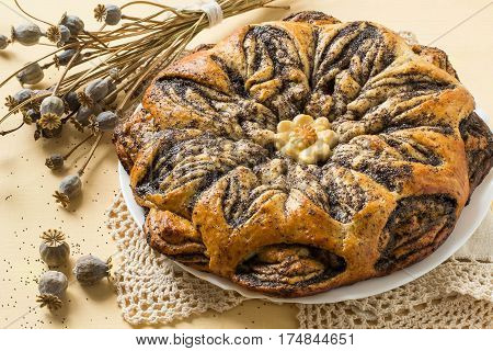 Creative homemade cakes from yeast dough. Original braided pie with poppy seeds and apples and dry poppy capsule with seeds on knitted napkin on yellow background