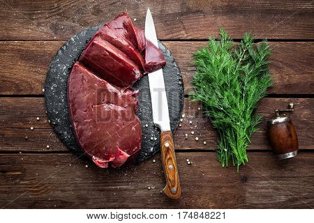 Raw liver on slate board on wooden background top view