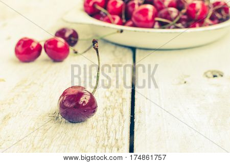 Red ripe juicy cherry in metal plate on white rustic wooden background. Sweet summer berries. Freshly harvested merry. Selective focus. Copy space.