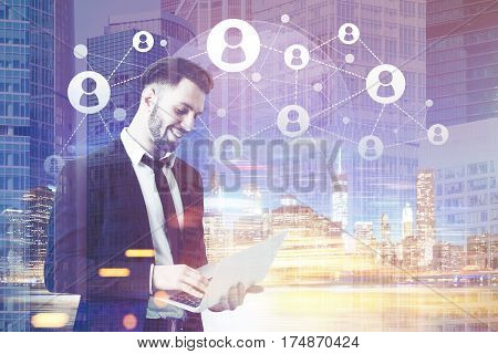 Portrait of a young bearded businessman working with his laptop in a large blue city. Network sketch in the sky. Toned image. Double exposure