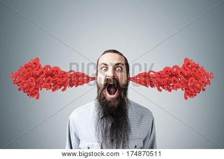 Portrait of an angry bearded man standing near a gray wall. There are two arrows made of question marks coming out of his ears.