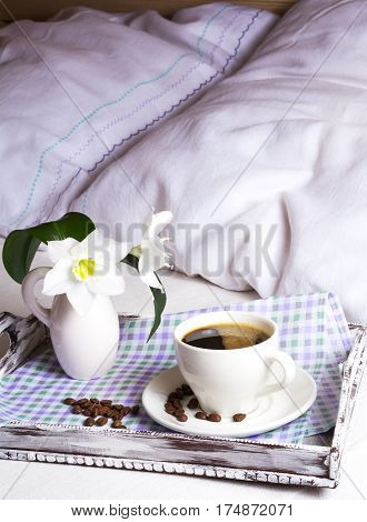Morning coffee in bed. Cup of fresh coffee with white lily flowers in vase on rustic wooden serving tray. Tender love concept.