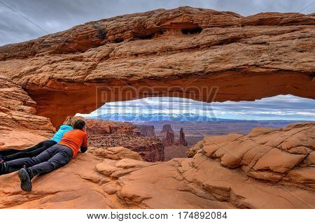 Friends enjoying the view of canyon and mountains. Mesa Arch. Canyonlands National Park. Moab. Utah. United States.