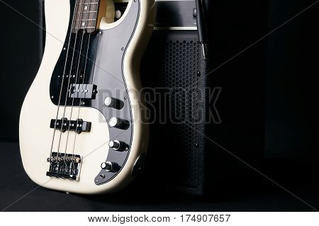 Black and white electric bass guitar with jack cable and classic amplifier on a dark background.Close up.