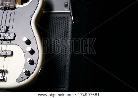 Black and white electric bass guitar with jack cable and classic amplifier on a dark background.Close up.