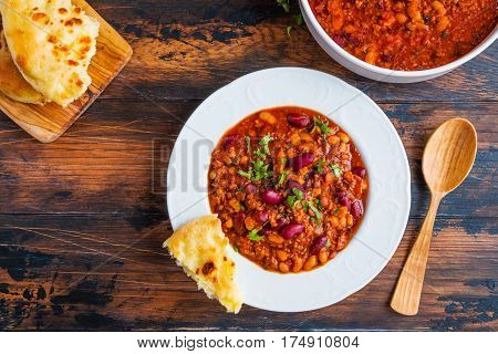 Traditional Polish dish stewed Breton beans with minced beef bacon mashed tomatoes onion garlic paprika bay leaves and spices. White plate and bread on wooden rustic table top view.